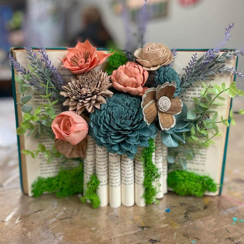 Decorative book with floral and succulent arrangements on a table.